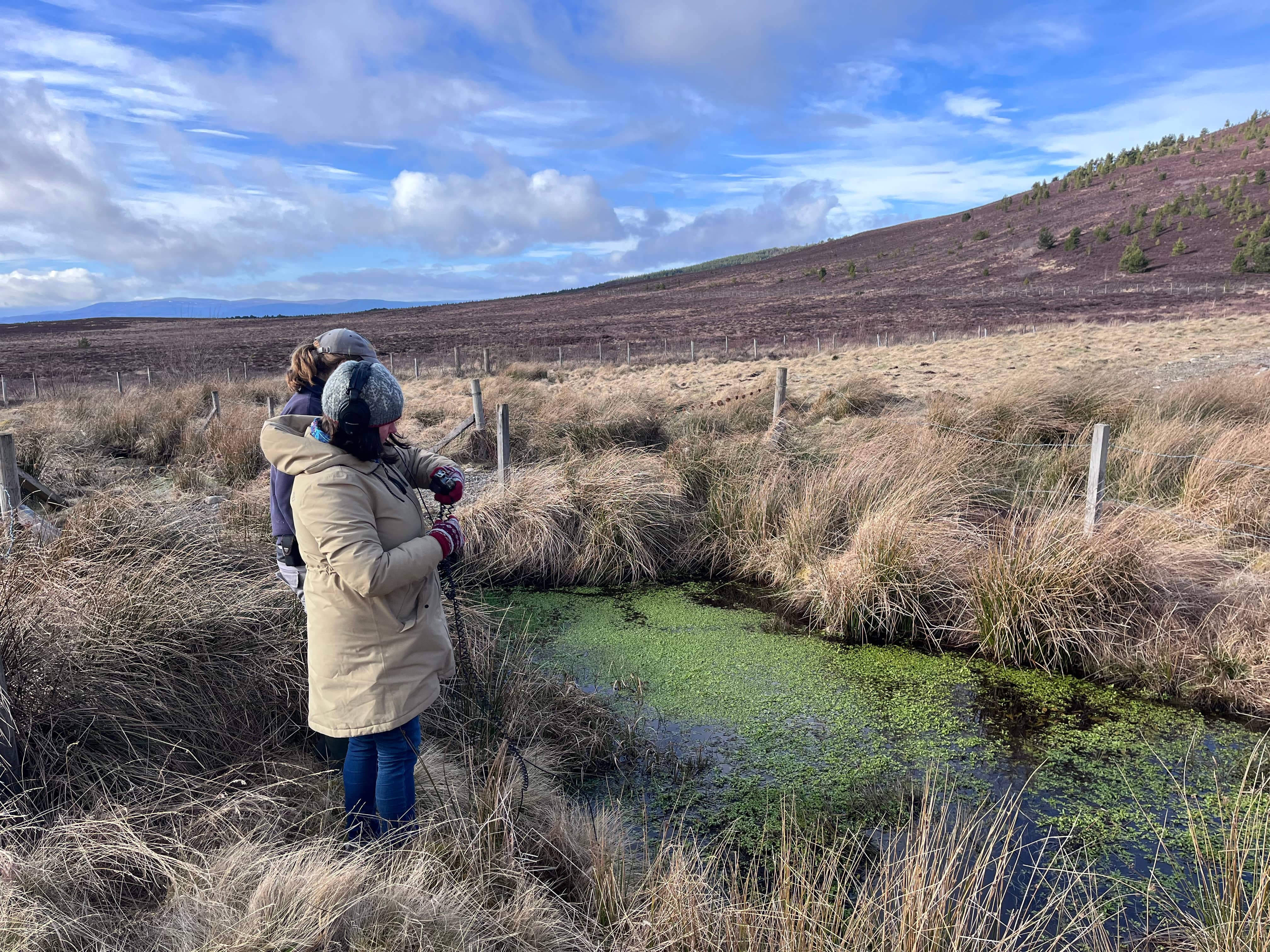 two people in a countryside setting with a pool of water in front of them.